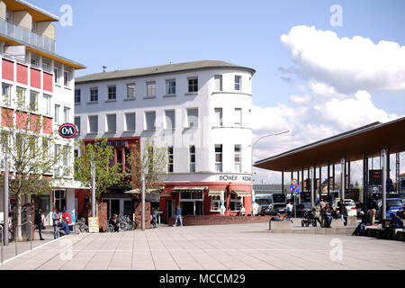 Rüsselsheim, Deutschland - 11 April 2018: Reisende und Passanten sitzen auf dem Bahnhofsvorplatz vor dem Hauptbahnhof sind in gutem Wetter Stockfoto