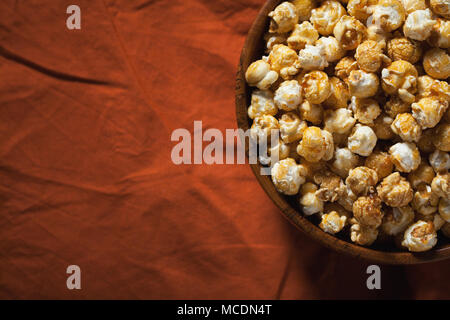 Hölzerne Schüssel mit süßem Popcorn auf orange Bettwäsche. Snacks und Essen für einen Film. Stockfoto