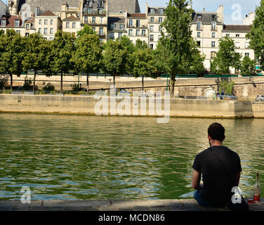 Ein Mann sitzt alleine mit einer Flasche Wein, entspannen Sie am Ufer der Seine in Paris. Stockfoto