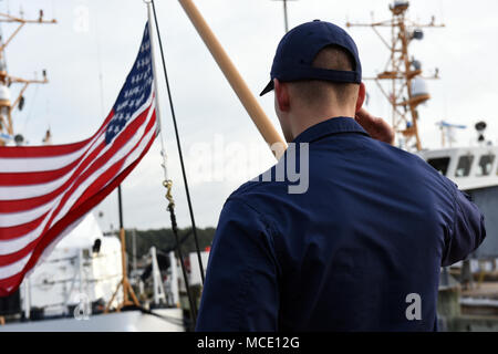 Coast Guard Seaman Jesse Adams, ein Mitglied der Besatzung an Bord Cutter fliegende Fische, begrüßt Nach dem Hissen der Flagge während der Morgen Farben bei gemeinsamen Expeditionary Base wenig Creek-Fort Geschichte in Virginia Beach, Virginia, Feb 15, 2018. Wenn im Hafen festgemacht, Coast Guard Cutter führen morgen Farben um 8 Uhr und abends Farben bei Sonnenuntergang jeden Abend. (U.S. Coast Guard Fotos von Petty Officer Corinne Zilnicki/Freigegeben) Stockfoto