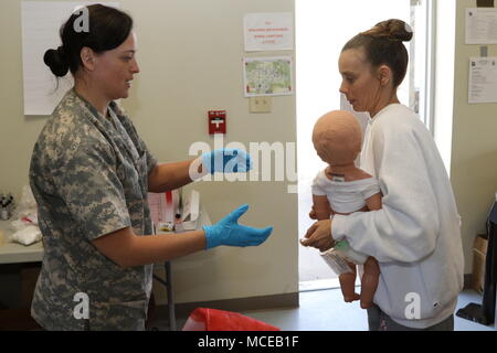 Spc. Jennifer Rosas, der Assistent eines Kaplan mit den 319 Signal Bataillon, in Sacramento, Calif., nimmt ein Baby Puppe aus einer Vertriebenen zivile Rolle Spieler zu malen simulieren brennt während Wächter Antwort 18 an muscatatuck Urban Training Center, Ind., 11. April 2018. Mehr als 4.500 Soldaten aus 80 Einheiten über dem Land beteiligen sich an Wächter Antwort 18. Dies ist eine multi-component Training mit aktiven - Aufgabe Elemente der XVIII Airborne Corps sowie Mitglieder des Michigan Army National Guard. (U.S. Armee finden Foto: Staff Sgt. Carolyn Hawkins) Stockfoto