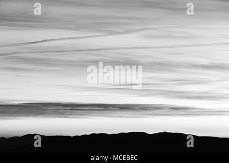 Sonnenuntergang über die Berge in der Ferne, mit tiefen Himmel voller Wolken und Kondensstreifen Stockfoto