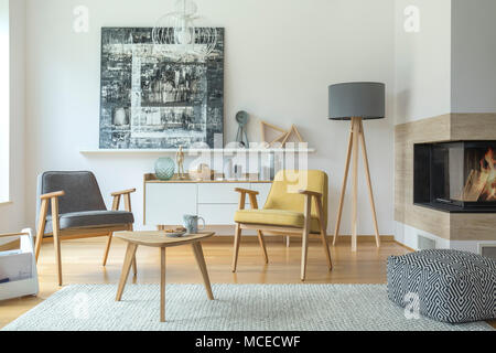 Grau und Gelb Holz Sessel im Wohnzimmer Einrichtung mit gemusterten Puff in der Nähe von Kamin und Lampe Stockfoto