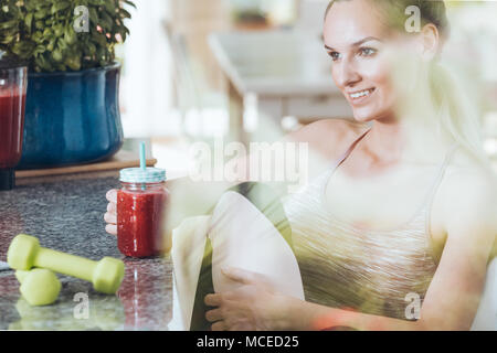 Junge Frau sitzt am Tisch und trink Smoothie nach Morgen Workout Routine Stockfoto