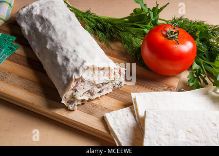 Dünne armenische Fladenbrot oder Lavash gewickelt Hüttenkäse oder Quark, Hühnerfleisch, Tomaten, Tomaten und Kräuter - Dill, Zwiebel, Petersilie auf Schneidebrett. Stockfoto