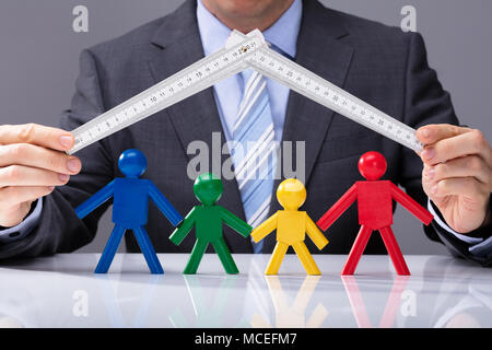 Der Geschäftsmann, der Hand, die eine Messung Klebeband über Mehrfarbige menschliche Figuren auf weißem Schreibtisch Stockfoto