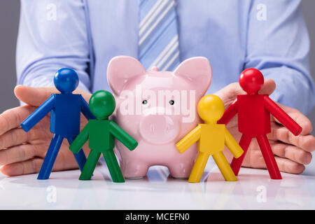 Nahaufnahme der Hand Schutz einer Person sparschwein und mit menschlichen Figuren Stockfoto