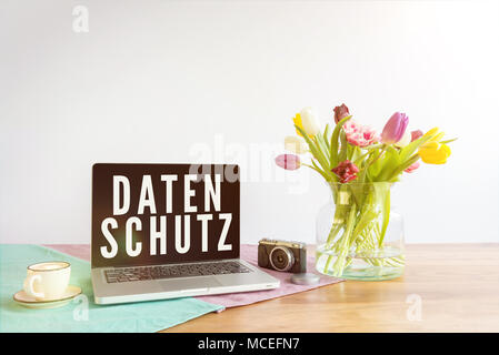 Deutsche Wort Datenschutz auf dem Laptop Bildschirm Sinne Datenschutz in Englisch auf hölzernen Schreibtisch mit Blumen vor weißem Hintergrund geschrieben Stockfoto