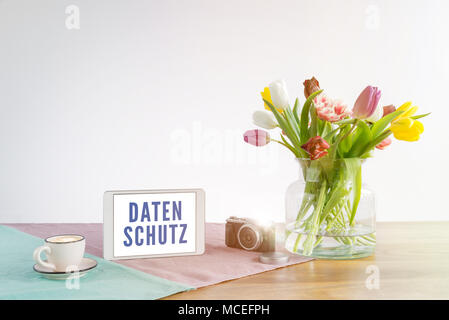 Deutsche Wort Datenschutz auf Tablet Bildschirm Sinne Datenschutz in Englisch auf hölzernen Schreibtisch mit Blumen vor weißem Hintergrund geschrieben Stockfoto