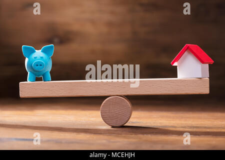 Auswuchten von Blauen Sparschwein und Miniatur Haus Modell auf der hölzernen Wippe Stockfoto