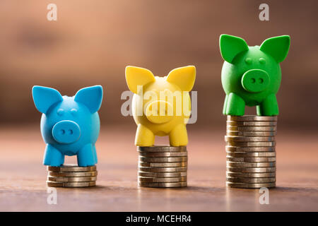 Reihe von bunten Sparschwein auf dem Stack der Erhöhung der Münzen über die hölzerne Schreibtisch Stockfoto