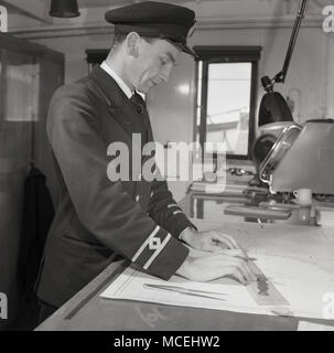 1950, historische, Zweiter Offizier oder den Navigator in seine Uniform an Bord das Deck eines Dampfers, der an den schifffahrtskarten genaue Position des Schiffes zu etablieren. Stockfoto