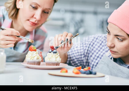 Junge konzentriert kaukasischen Frauen Cupcakes dekorieren Creme mit frischen Erdbeeren, Heidelbeeren und Johannisbeeren Stockfoto