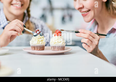 Nahaufnahme der kaukasischen Frauen freundlich lächelnd, während Dekorieren appetitlich cream Cupcakes mit Beeren- und Eisbildung Stockfoto