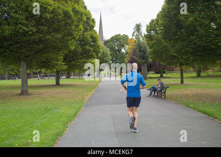 Ein junger Mann joggt im Sommer durch Clissold Park, Stoke Newington, London N 16, mit der St. Mary's Kirche im Hintergrund Stockfoto