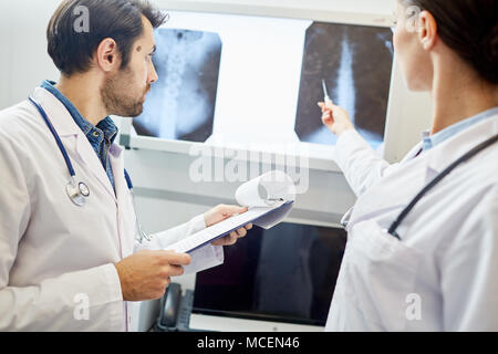 Männlicher Arzt mit Zwischenablage Hören seines Kollegen sprechen über x-ray Stockfoto