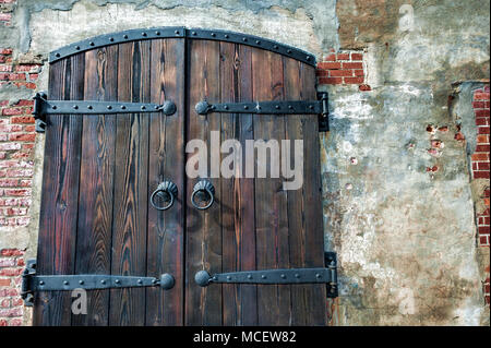 Nahaufnahme eines schwere hölzerne Anlage Doppeltür, mit Eisen Scharniere und Griffe, verschließen den Eingang in einem alten Backsteingebäude. Stockfoto