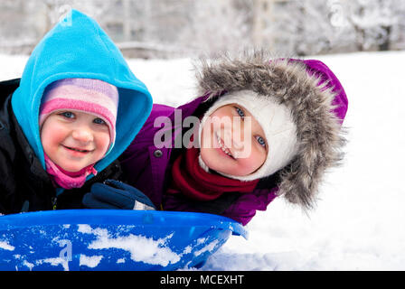 Zwei Schwestern auf Schlitten, lächelnd und Spaß im Winter spielen. Stockfoto