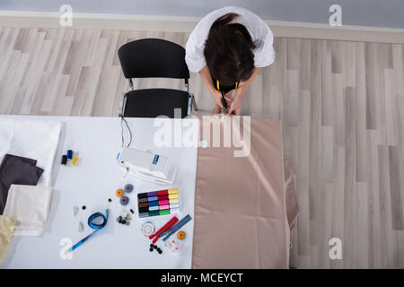 Junge weibliche Mode Designer Schneiden Tuch mit der Schere auf dem Schreibtisch im Studio Stockfoto