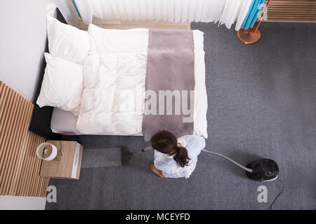 Glückliche junge Haushälterin Reinigung Teppich mit Staubsauger im Hotel Zimmer Stockfoto