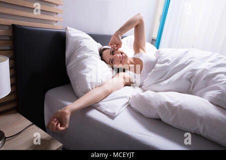 Lächelnden jungen Frau liegend auf Bett im Schlafzimmer Stockfoto