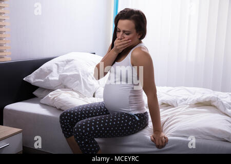 Seitliche Sicht auf eine junge Frau sitzt auf dem Bett im Schlafzimmer Stockfoto