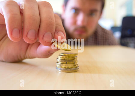 Ein Mann zählt seine Münzen auf einen Tisch. Bei den Männern sind die Hände sanft die Münze auf der Münze stack. Konzept der Geld sparen und finanziell zu wachsen. Stockfoto