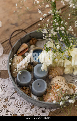 Küsten- oder rustikalen Interieur Design Konzept. Tabelle Mittelstück mit Metall Tablett mit Kerzen, Muscheln und Blumen. Stockfoto