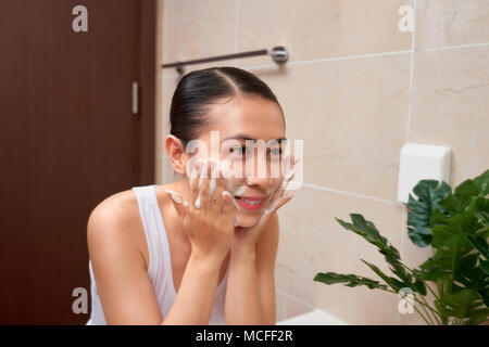 Junge schöne asiatische Frau waschen Ihr Gesicht mit den Händen von Soap Stockfoto