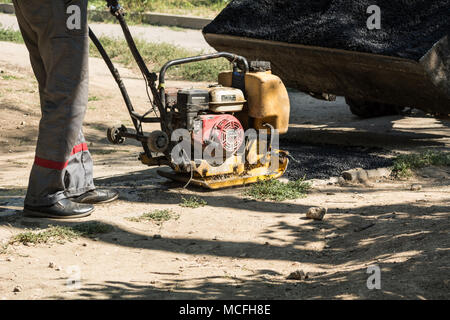 Straße zur Reparatur. Ein Arbeitnehmer, der mit einem manuellen Fertiger richtet die heißen Asphalt auf der Straße. Stockfoto