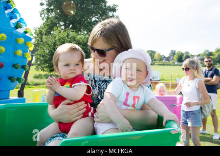 Eine junge Mutter mit Zwillingsbabys auf ihrem ersten Fairground Ride, Großbritannien Stockfoto