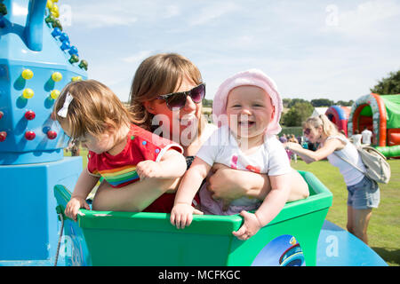 Eine junge Mutter mit Zwillingsbabys auf ihrem ersten Fairground Ride, Großbritannien Stockfoto