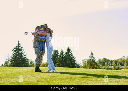 Glückliche Wiedervereinigung der Soldat mit der Familie im Freien. Militärischen Mann seine Familie, die auf den Park Rasen. Stockfoto