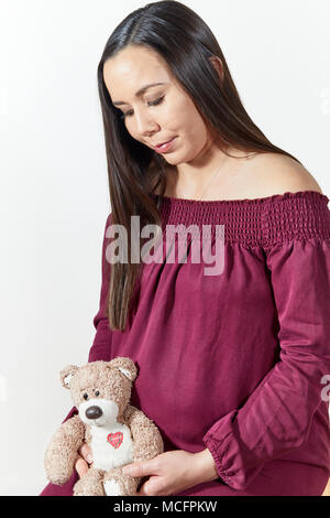 Attraktive schwangere Frau Holding ein Ausgestopfter Teddybär und lächelnd auf Weiß isoliert Stockfoto