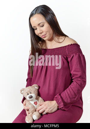 Attraktive schwangere Frau Holding ein Ausgestopfter Teddybär isoliert auf weißem Stockfoto