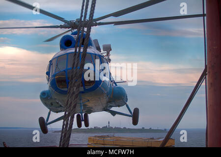 Schiff Hubschrauber, Landung auf dem Landeplatz am Heck des Schiffes, auf dem Hintergrund der Insel und Leuchtturm, Be- und Entladen. Hubschrauber macht Eis Stockfoto