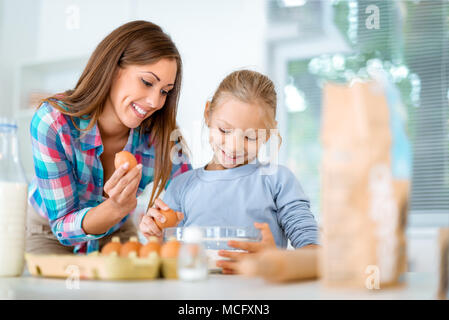 Mutter und kleine Mädchen rissen Eier für den Teig in der heimischen Küche zu Mehl. Mutter lernt ihre Tochter, wie die Cookies zu machen. Stockfoto