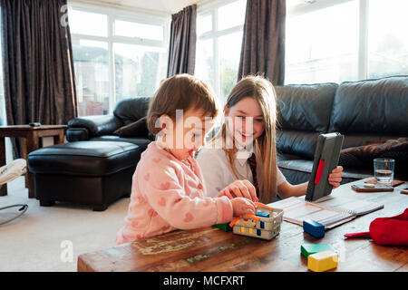 Kleines Mädchen lenkt Ihre ältere Schwester, während Sie zu Hause zu studieren. Sie spielen mit Spielzeug Bausteine zusammen. Stockfoto