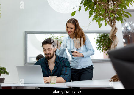 Junge erfolgreiche Designer arbeitet an einem Laptop und das Sprechen über dieses Projekt im Büro während der Kaffeepause. Stockfoto