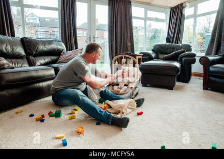Bleiben Sie zu Hause, Vater ist entspannend im Wohnzimmer mit seiner Tochter, während Sie in Ihrem Baby Bouncer ist. Stockfoto