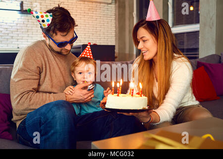 Eltern mit einem Kuchen mit Kerzen gratulieren ihr Kind an seinem Geburtstag. Stockfoto