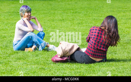 Zwei junge Frauen sitzen Spaß auf dem Rasen der Royal Pavilion, Brighton, East Sussex, England Großbritannien im April Stockfoto