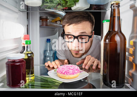 Man schaut auf einen Donut im Kühlschrank. Stockfoto