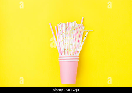 Gestapelte Rosa trinken Pappbecher mit gestreiften Strohhalme auf gelben Hintergrund. Flach Komposition. Geburtstag Feier Kinder Spaß. Freundliche Atmosph Stockfoto