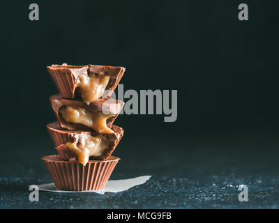 Stapel von vegane Schokolade Tassen mit Karamell auf dunklen Tischplatte. Hausgemachte vegetarische Chocolate Caramel Cups mit rohem Kakao Schokolade. Ideen und Rezepte fo Stockfoto