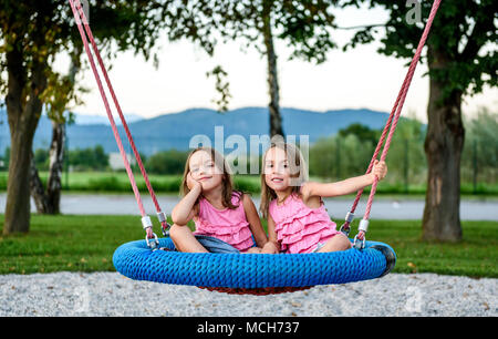 Zwilling Mädchen auf Spinnennetz nest Schaukel auf dem Spielplatz. Aktive Kinder spielen mit Giant Swing-N-Folie Monster Web Schwingen am Spielplatz im Freien Stockfoto