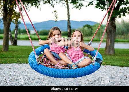 Zwilling Mädchen auf Spinnennetz nest Schaukel auf dem Spielplatz. Aktive Kinder spielen mit Giant Swing-N-Folie Monster Web Schwingen am Spielplatz im Freien Stockfoto