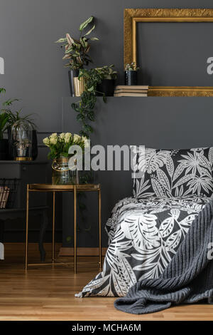 Weiße Rosen auf Gold Tisch im gemütlichen grau Schlafzimmer Einrichtung mit gemusterter Bettwäsche auf dem Bett Stockfoto