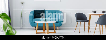 Blaues Sofa mit dekorativen Kissen und weiß Couchtisch mit Glas Kerzenhalter in Wohnzimmer Innenraum Stockfoto