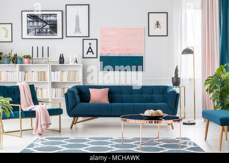 Modernes Wohnzimmer Innenraum mit blauen Sofa, Teppich, Kunstsammlung und rosa Details Stockfoto
